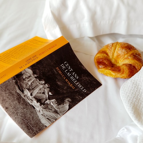 Cent ans de Laurelfield - roman de Rebecca Makkai Roman "Cent ans de Laurelfield " de Rebecca Makkai posé ouvert sur le lit avec un croissant à portée de main