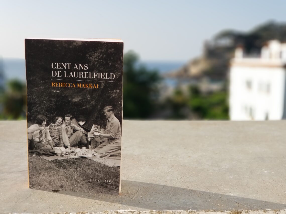 Livre "Cent ans de Laurelfield" de Rebecca Makkai posé sur le rebord du balcon surplombant la mer
