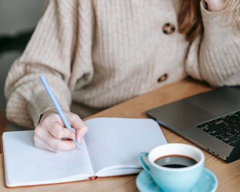 Le Code Talent de Daniel Coyle : prendre des notes pour devenir meilleur Jeune femme qui prend des notes sur un carnet devant son ordinateur avec une tasse de café posée devant elle.