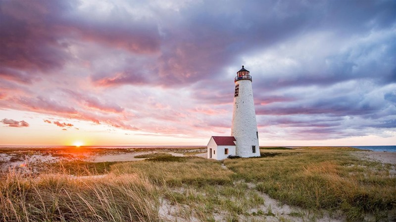 le Phare Great Point sur l'île de Nantucket le Phare Great Point sur l'île de Nantucket avec le soleil qui se couche à l'horizon et le vent qui courbe les herbes sur le sable