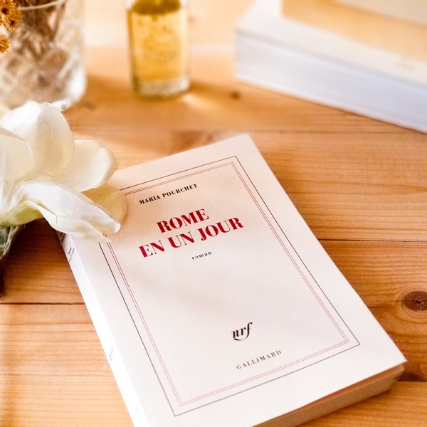 Rome en un jour - Maria Pourchet le livre "Rome en un jour" de Maria Pourchet posé en gros plan sur une table en bois avec une fleur flanche.