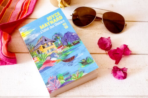 Photo du livre "L'hôtel des oiseaux" de Joyce Maynard posé sur une table en bois blanc avec lunettes de soleil et fleurs de bougainvilliers rose